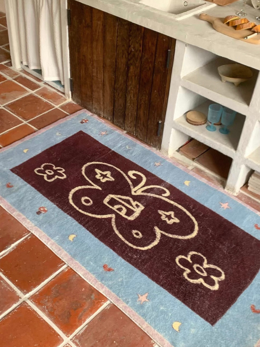A Kawaii rug with a cream butterfly outline, flowers and a blue border lies beside open shelving.
