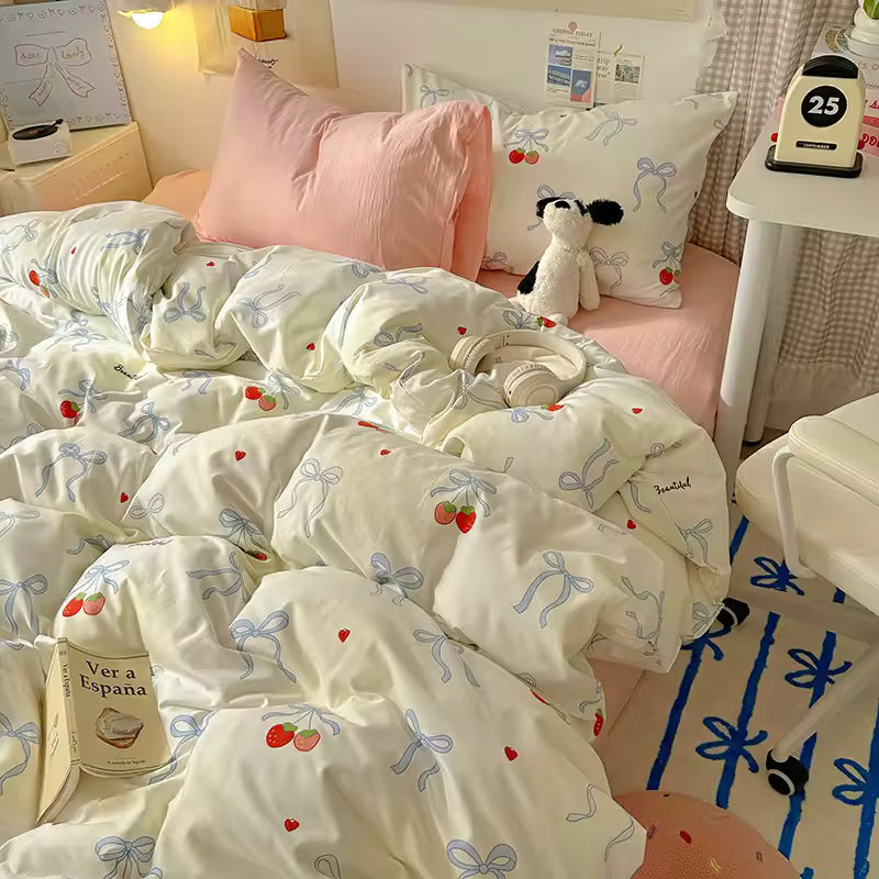 Bed with white bedding featuring red cherries and blue bows, pink pillow, and small plush toy.