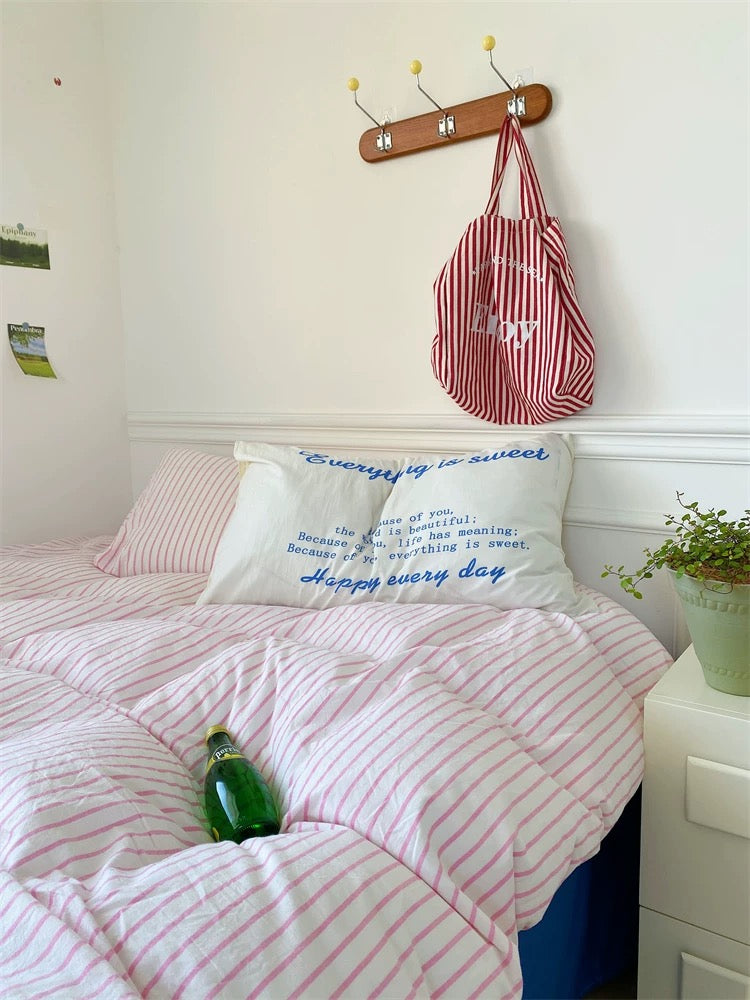 Bedroom with pink and white striped bedding, a pillow with text, and a red and white bag hanging on a hook.