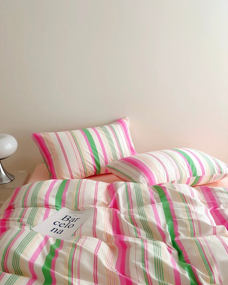 Striped bedding with pink and green lines on a bed against a plain wall.