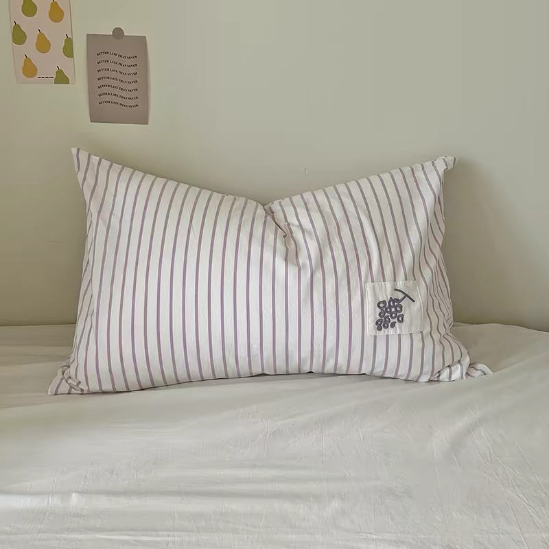 Purple striped pillowcase with an embroidered grape applique patch on a white bed.