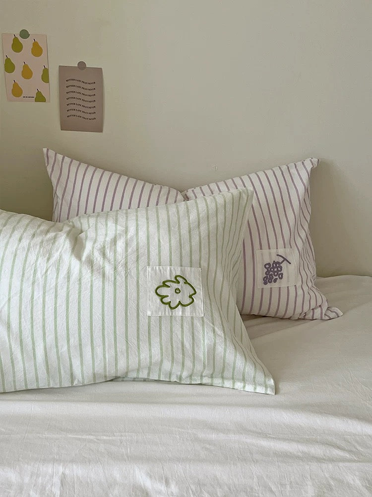 Lavender grape striped pillowcase beside sage flower striped pillowcase on white bedding.