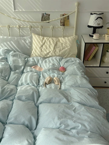 Light blue textured comforter on a bed with pillows and a nightstand in the background.