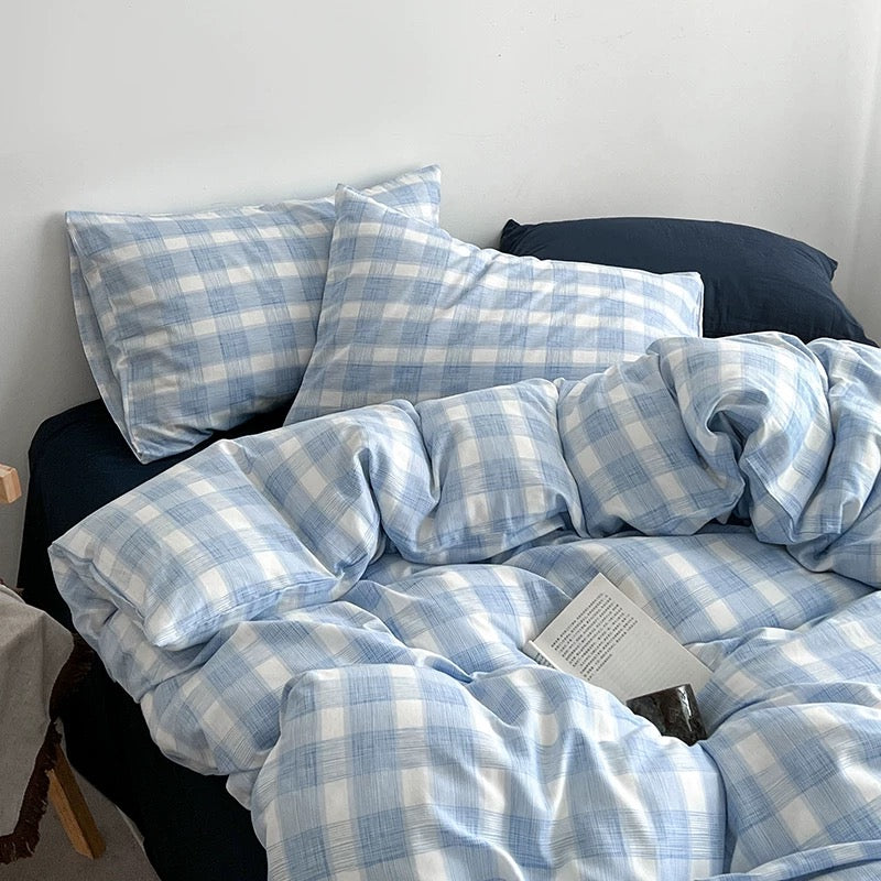 Light blue and white gingham check bedding set with matching pillowcases and a duvet cover, styled on a bed with dark navy pillows and sheets in a minimalist bedroom setting.