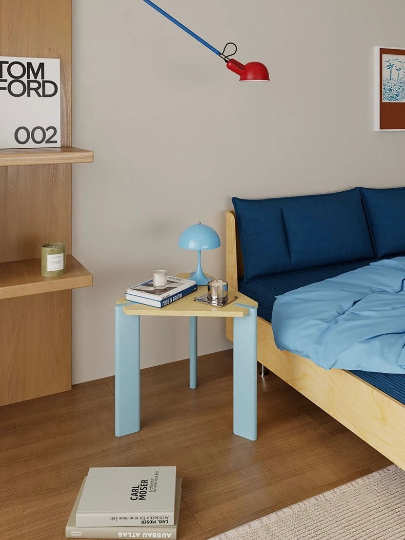 Light blue side table shown closer beside a blue bed, with a dome lamp and small objects on the wood top.