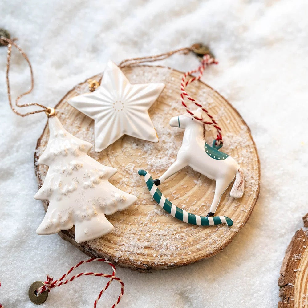 Metal Christmas ornaments show a white star, a white tree and a rocking horse with teal details.