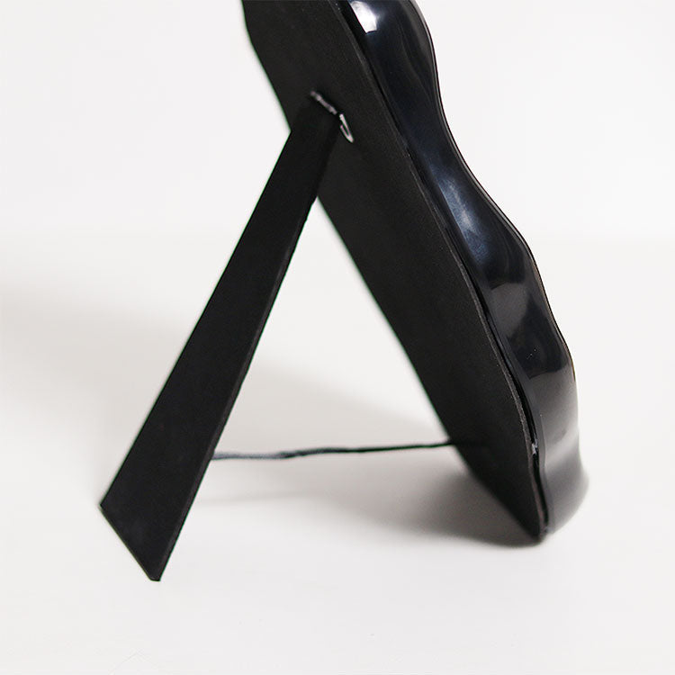 A close-up of a glossy black picture frame with its stand extended, set against a plain white background.