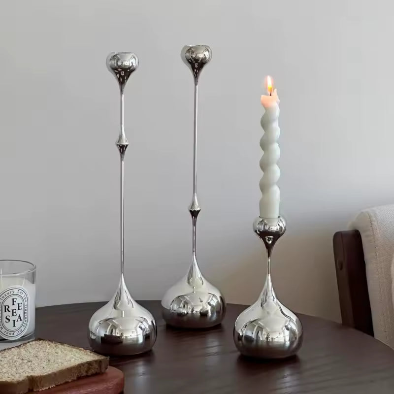 Three silver candle holders on a table with a lit candle and a glass of milk.