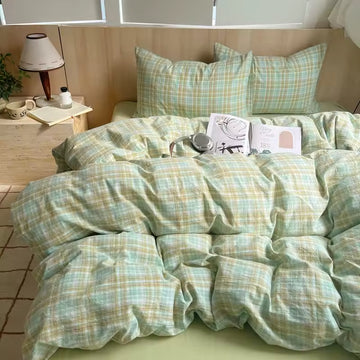 Bed with green plaid bedding, book, and headphones on a wooden floor.