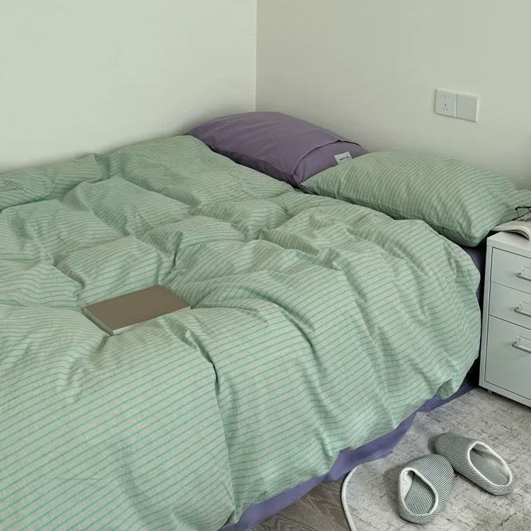 Bed with green striped bedding and a purple pillow in a room.