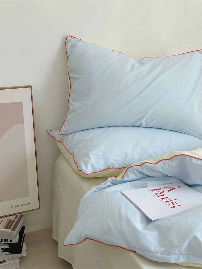 Light blue comforter with red trim on a bed in a bedroom setting.