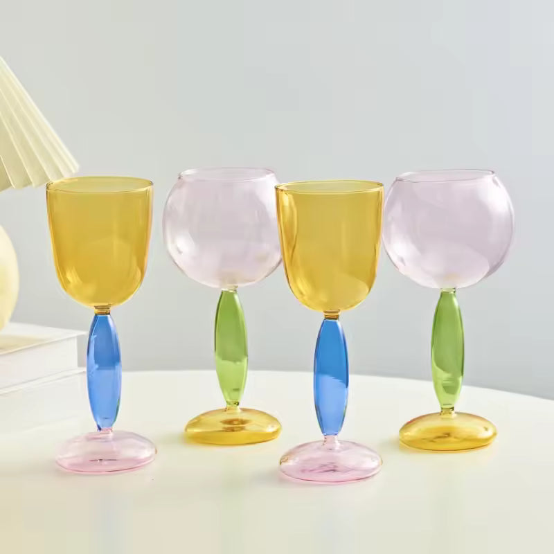 Set of four colorful wine glasses with multicolored stems on a light background