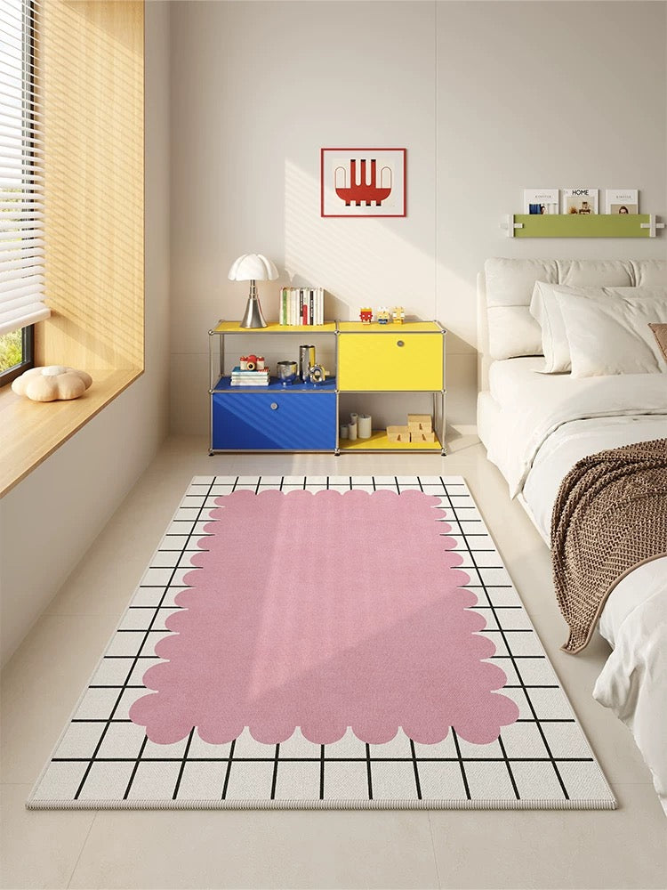 Modern bedroom with a pink and white geometric rug, colorful storage unit, and bed with pillows.