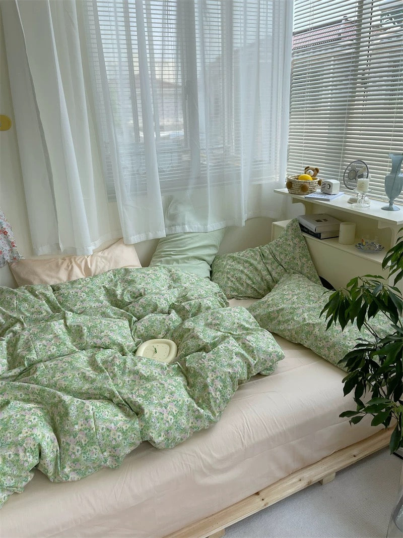 Bed with green floral bedding in a room with white curtains and a desk.