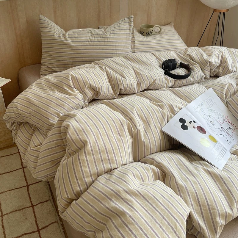 Beige striped bedding on a bed with a lamp and pillow in the background.
