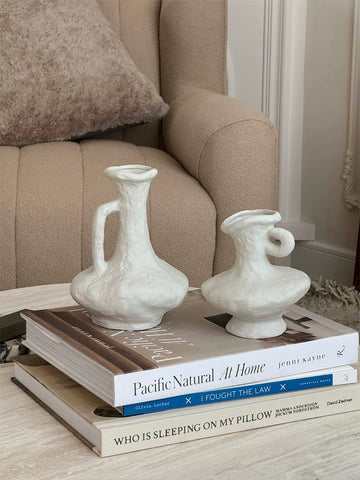 Two white ceramic vases on a stack of books with a beige sofa in the background