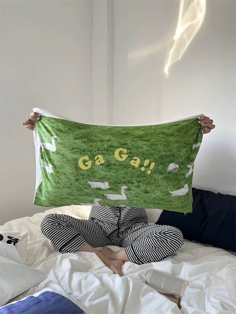 Person holding a green towel with duck designs and 'Ga Ga!!' text on a bed.