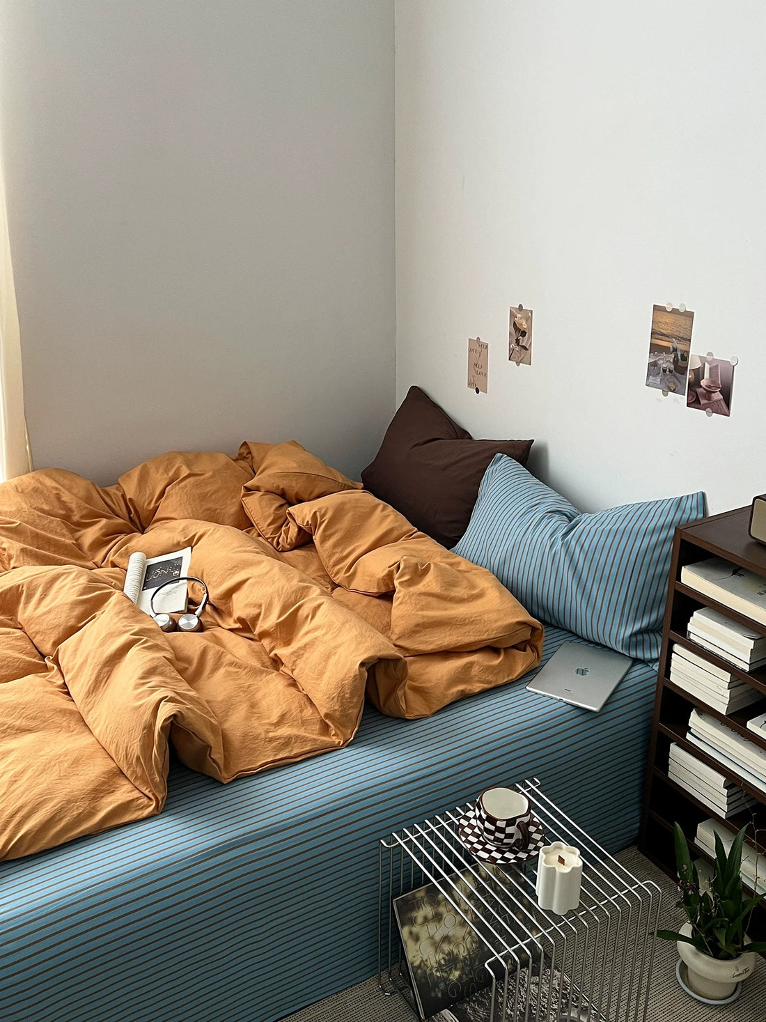 Orange bedding set with a blue striped sheet and brown pillow in a small bedroom