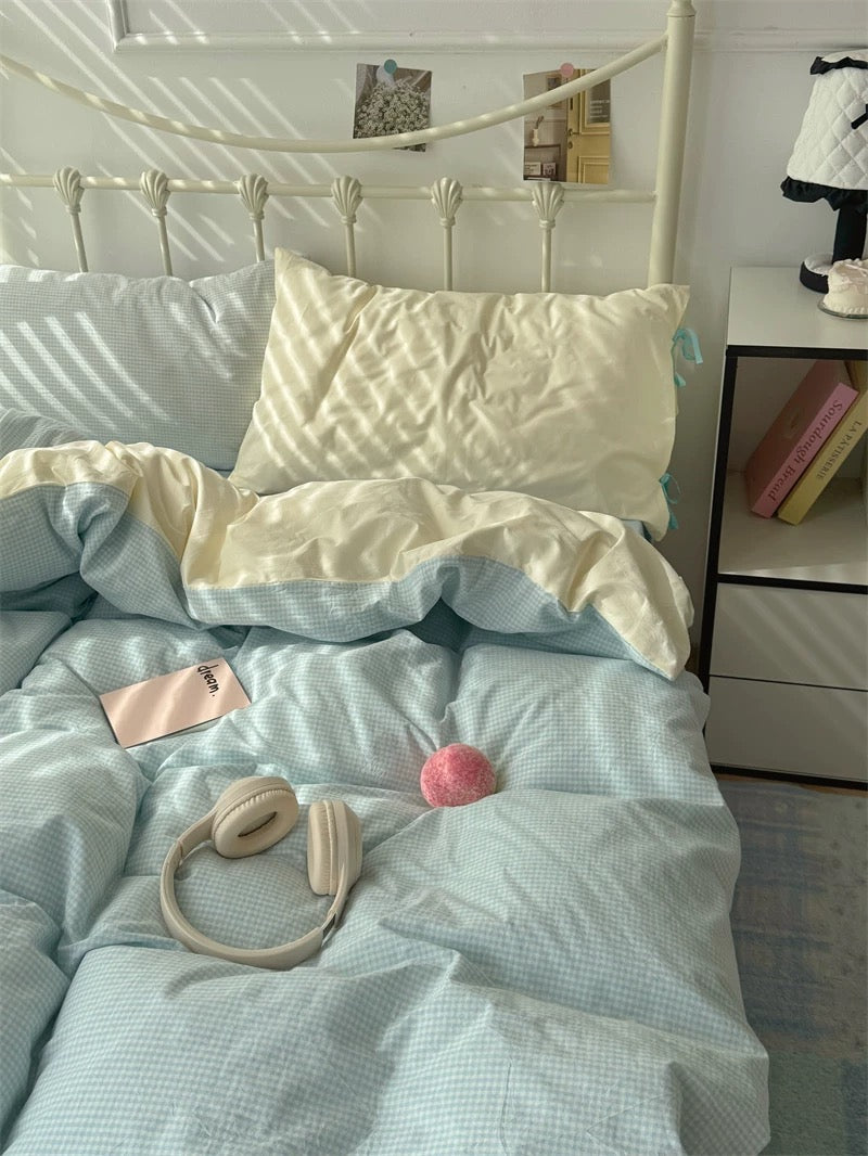 Bed with light blue bedding, white pillowcases, and a pink ball on a nightstand.