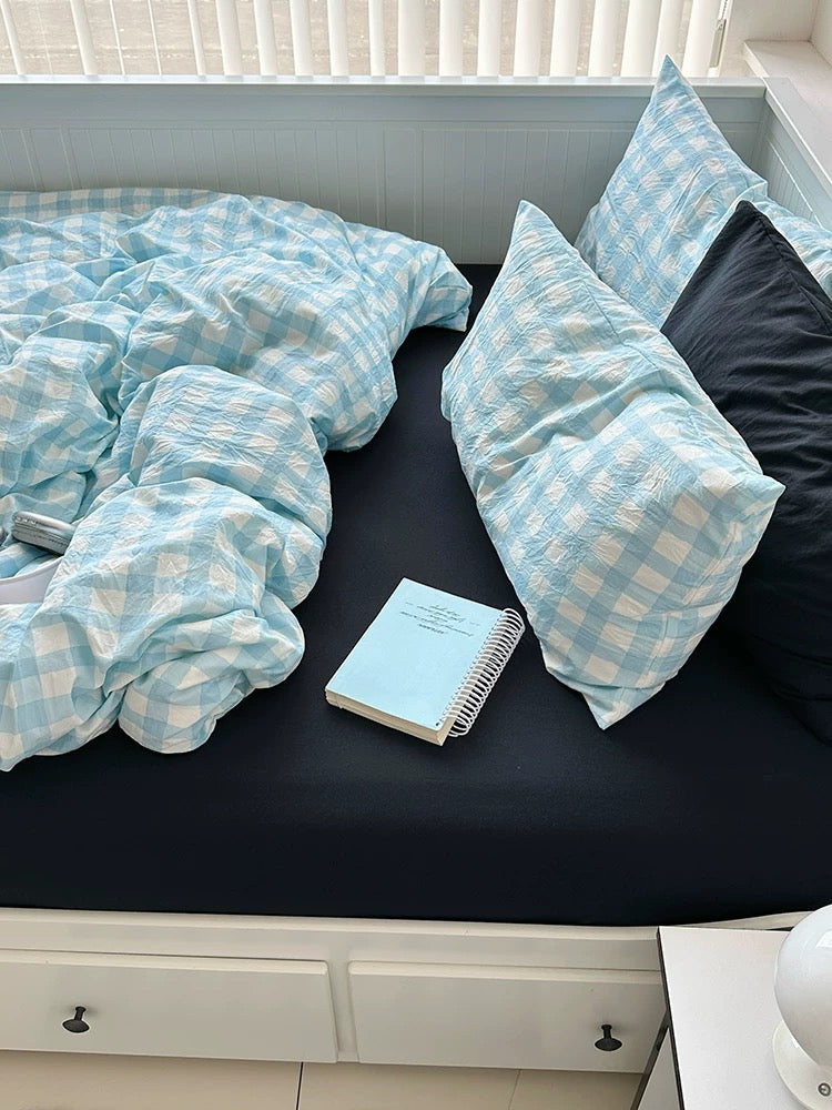 Bed with blue checkered bedding and pillows, featuring a notebook on the bed.