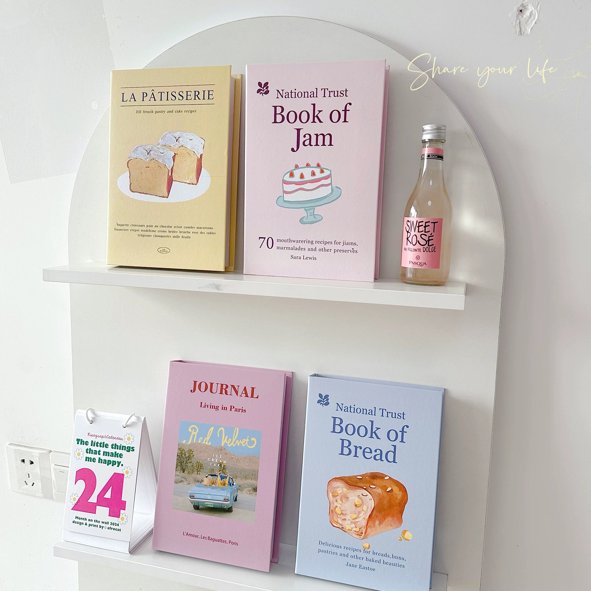 Shelf with books and a bottle of Sweet Rose on a white wall