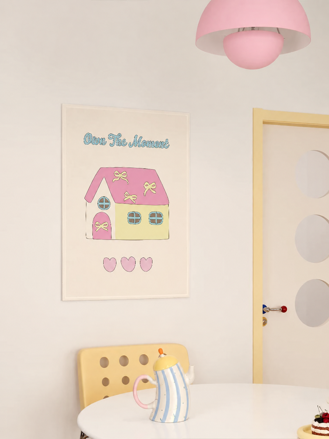 A house tapestry with a green house, pink roof and yellow hearts hangs above a small breakfast table.