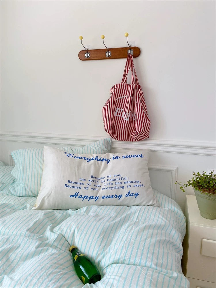 Bedroom with a pillow featuring text, a striped bag on a hook, and a bottle on the bed.