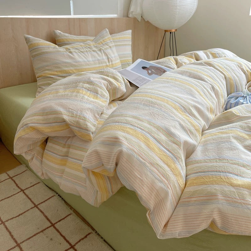Striped bedding on a bed with a magazine underneath, in a room with a tiled floor.