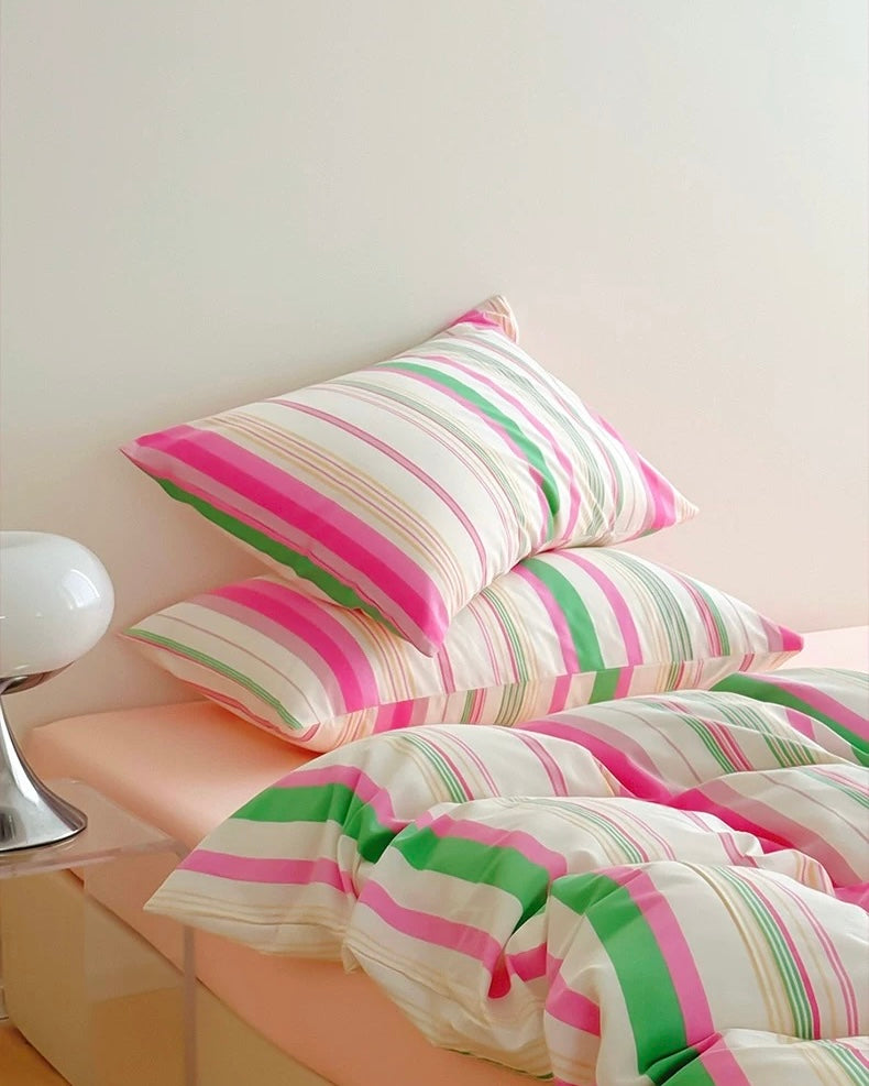 Striped pink and green bedding set on a bed with a white nightstand.