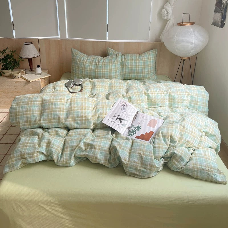 Bed with green plaid bedding, book, and headphones on a wooden floor.