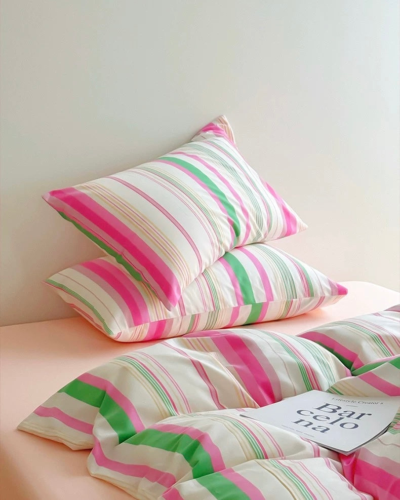 Striped pink, green, and white bedding with pillows on a bed.