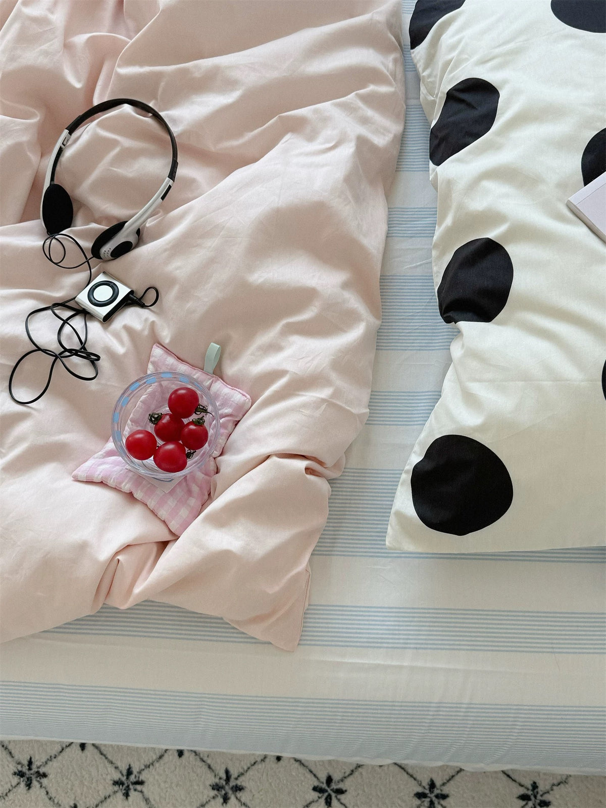 Close view of a large black dot pillowcase beside the pink duvet cover, striped sheet and headphones.