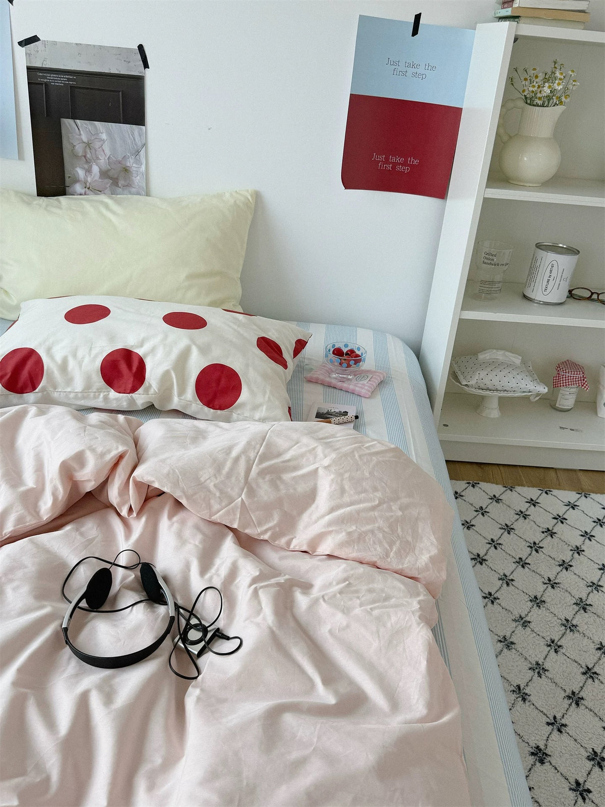 Pink bedding seen from the foot of the bed with a large red dot pillowcase and pale yellow pillow.