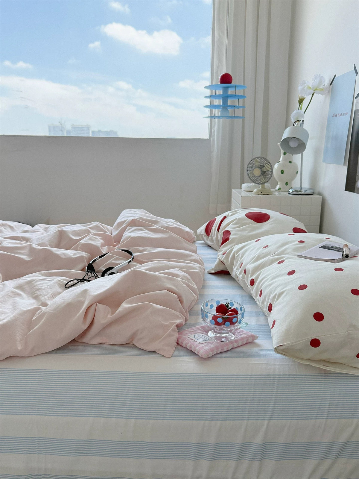 Side view of the pink bedding and red dot pillowcases beside a bright window.