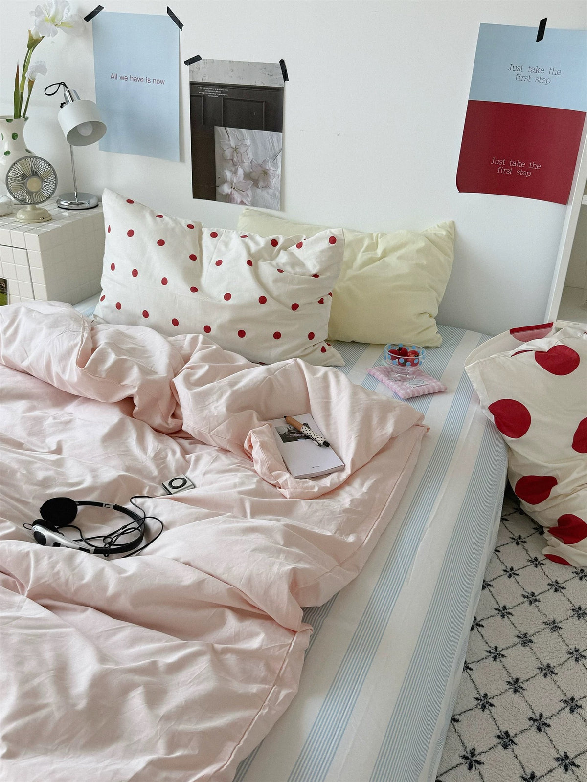Pink bedding with a pale yellow pillow and small red dot pillowcase, viewed from the foot of the bed.