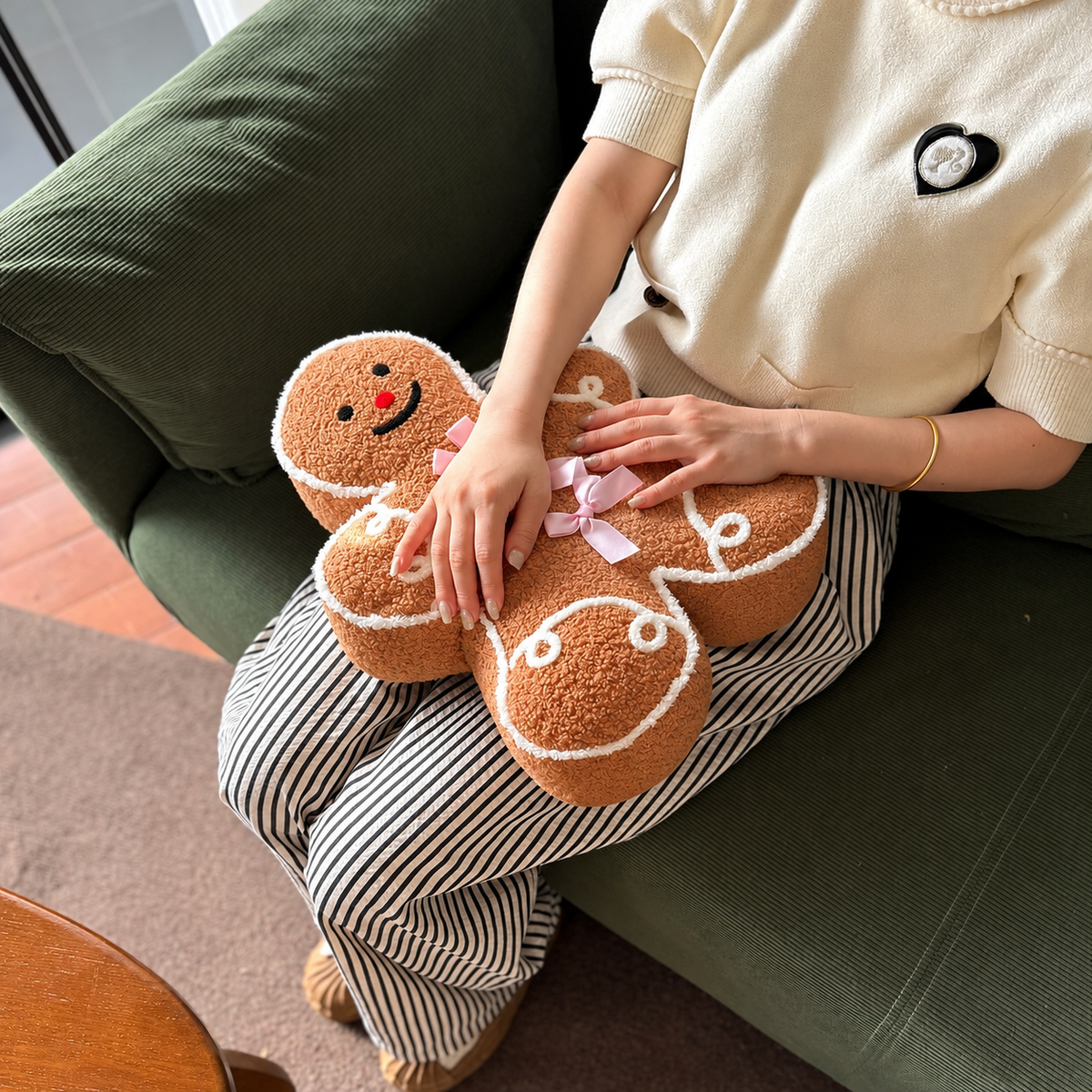 Pink bow gingerbread man Christmas pillow held up in a cozy living room