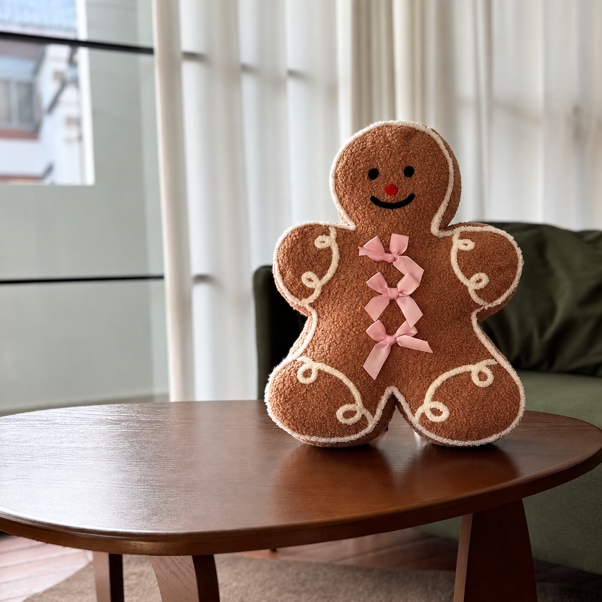 Gingerbread man shaped Christmas pillow with pink ribbon bows displayed on a round wooden table