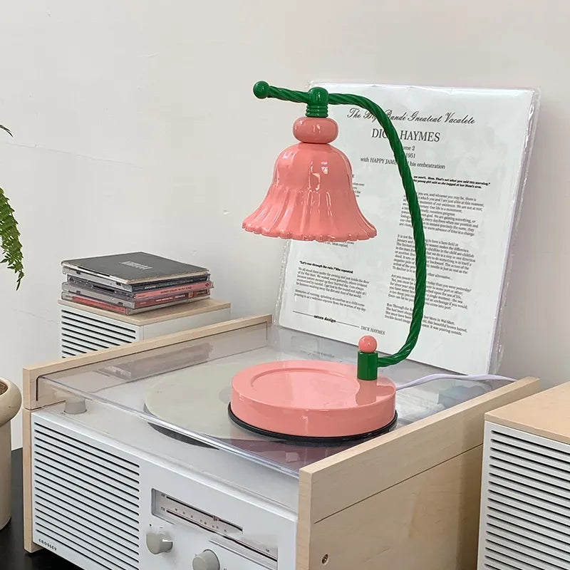 Pink flower candle warmer with a curved green stem, resting on an open record player.