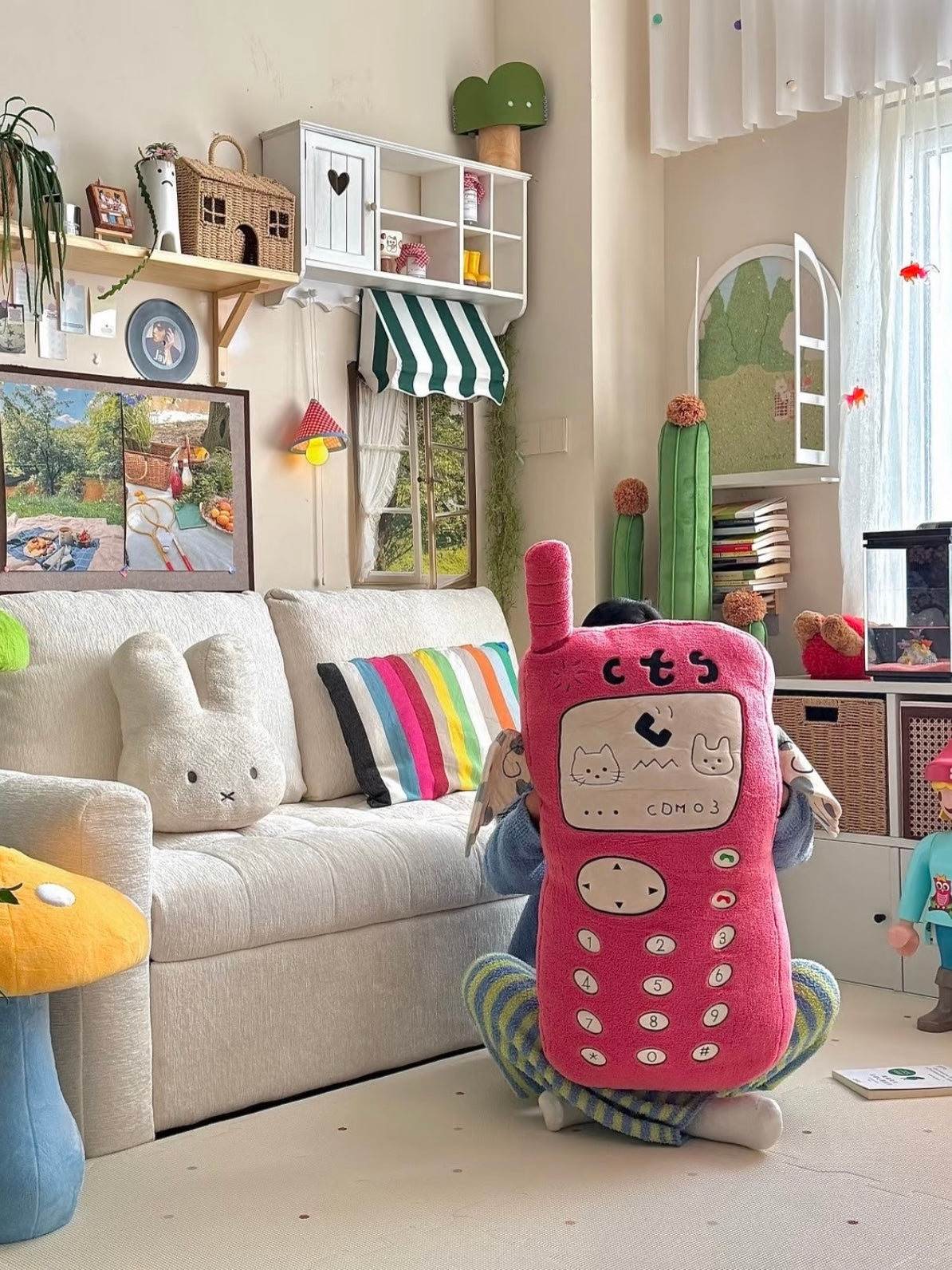 A pink phone pillow stands upright beside a sofa, with its spotted fabric arms extending out at both sides.
