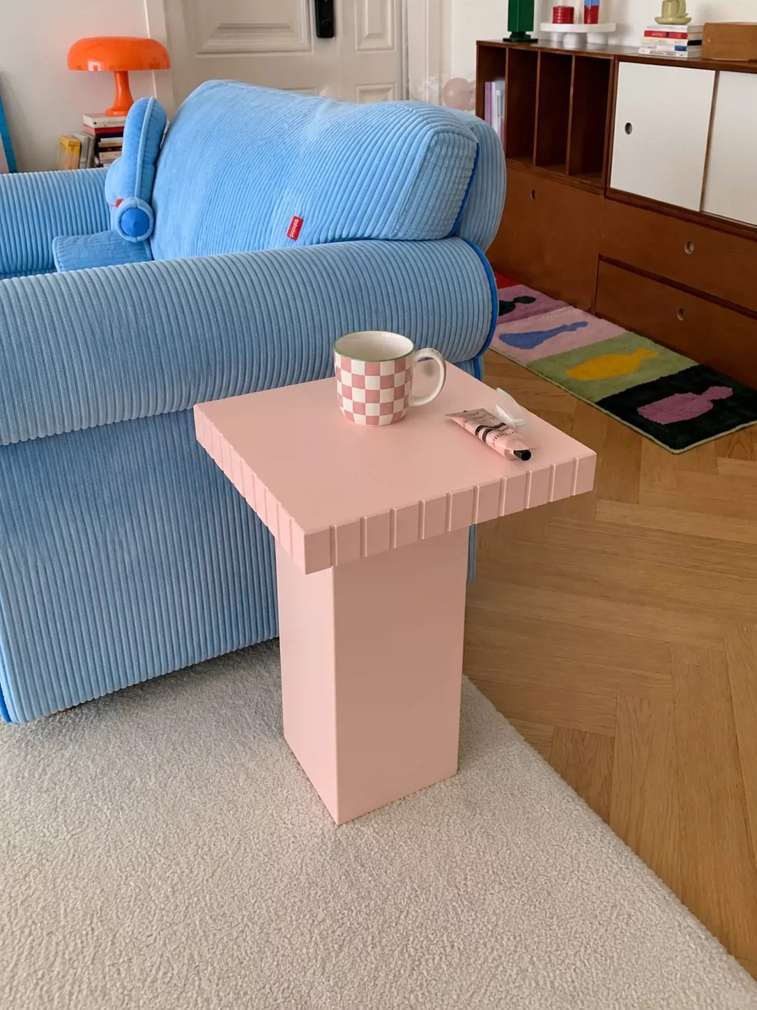 Pink side table with a speckled mug on a book next to a blue corduroy armchair