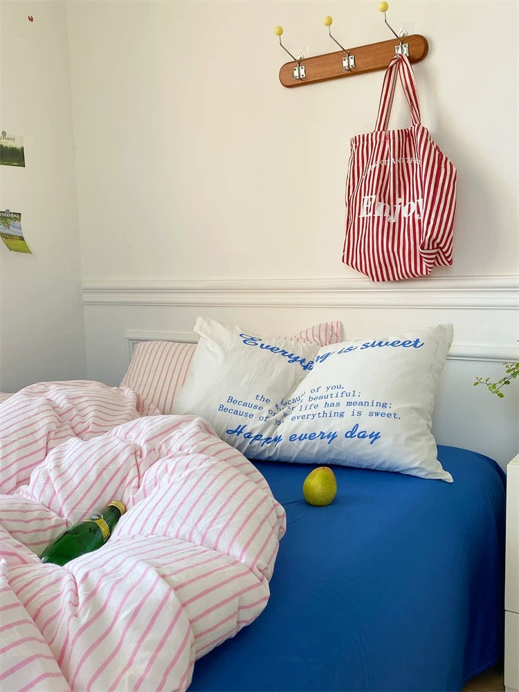 Bedroom with a bed featuring striped bedding and pillows, a red and white bag hanging on a hook above.