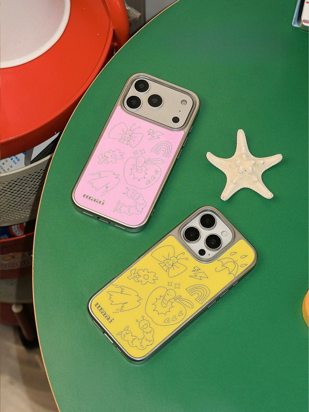Pink and yellow phone case options arranged diagonally, showing matching silver outline artwork.