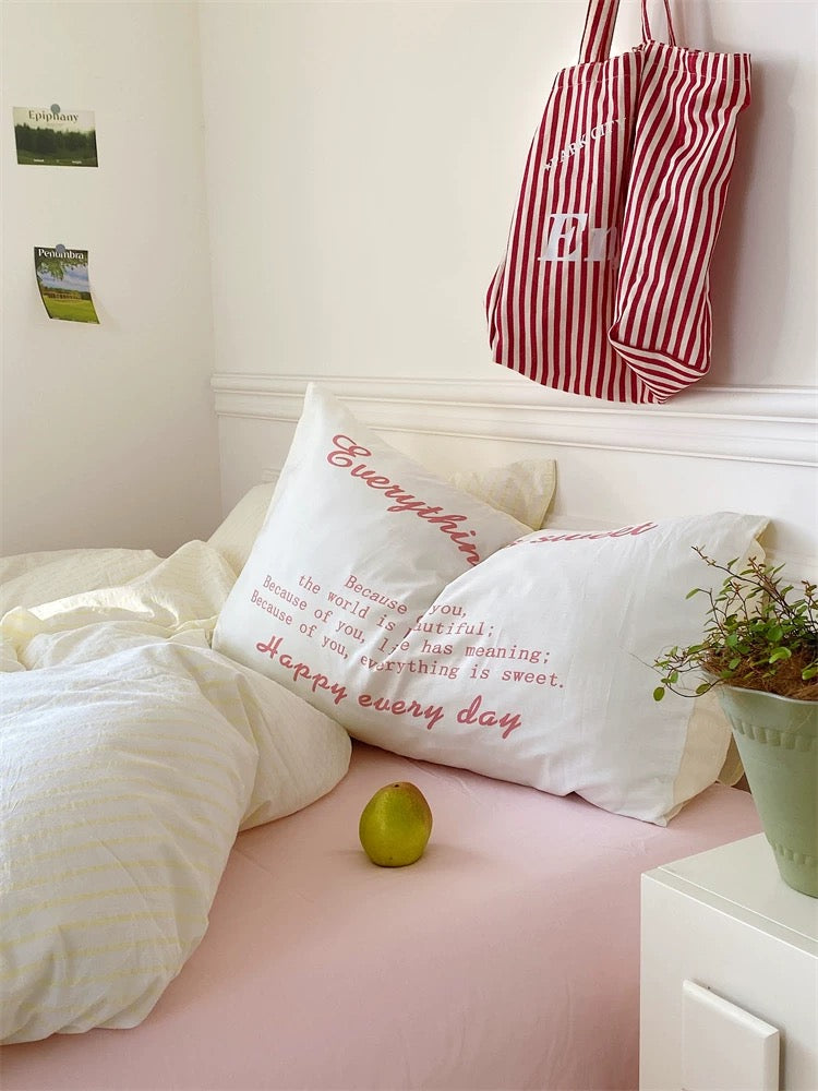 Bedroom with pillows, a lime, and a striped bag on a white bed.