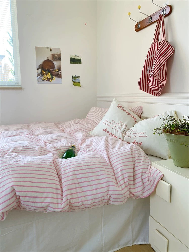 Bedroom with pink striped bedding, white pillows, and a plant on a nightstand.