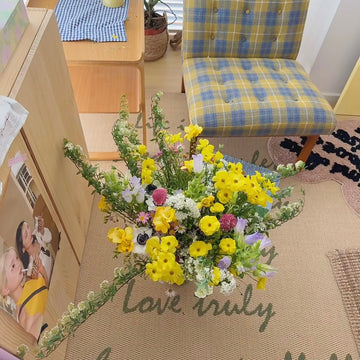 Bouquet of flowers on a floor with a checkered chair and wooden desk in the background.
