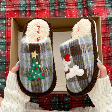 Blue plaid Christmas tree slippers with puppy motif held against a red tartan background