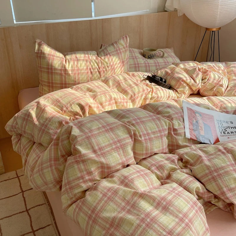 Bed with pink and yellow plaid bedding in a room with wooden walls and a lamp.