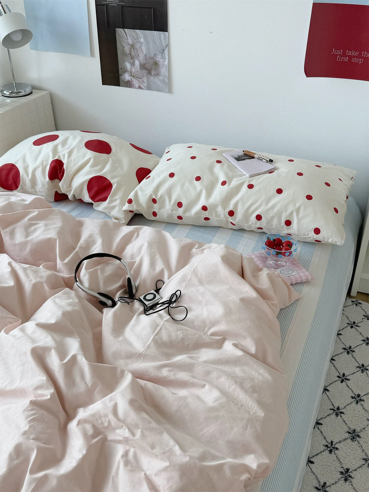 Small and large red dot pillowcases are paired above a rumpled pink duvet cover and striped sheet.