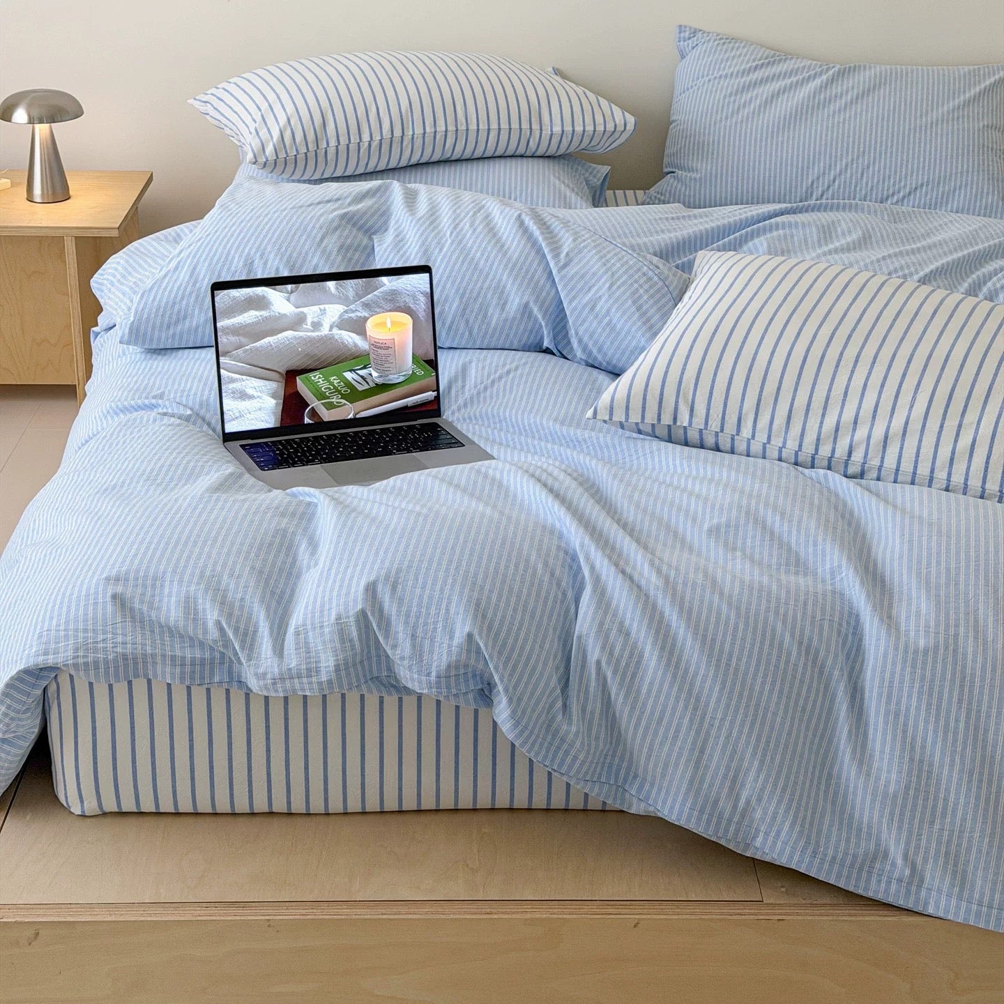 Powder blue bedding featuring fine white pinstripes creating airy minimalist sleep space with layered cotton comfort indoors.