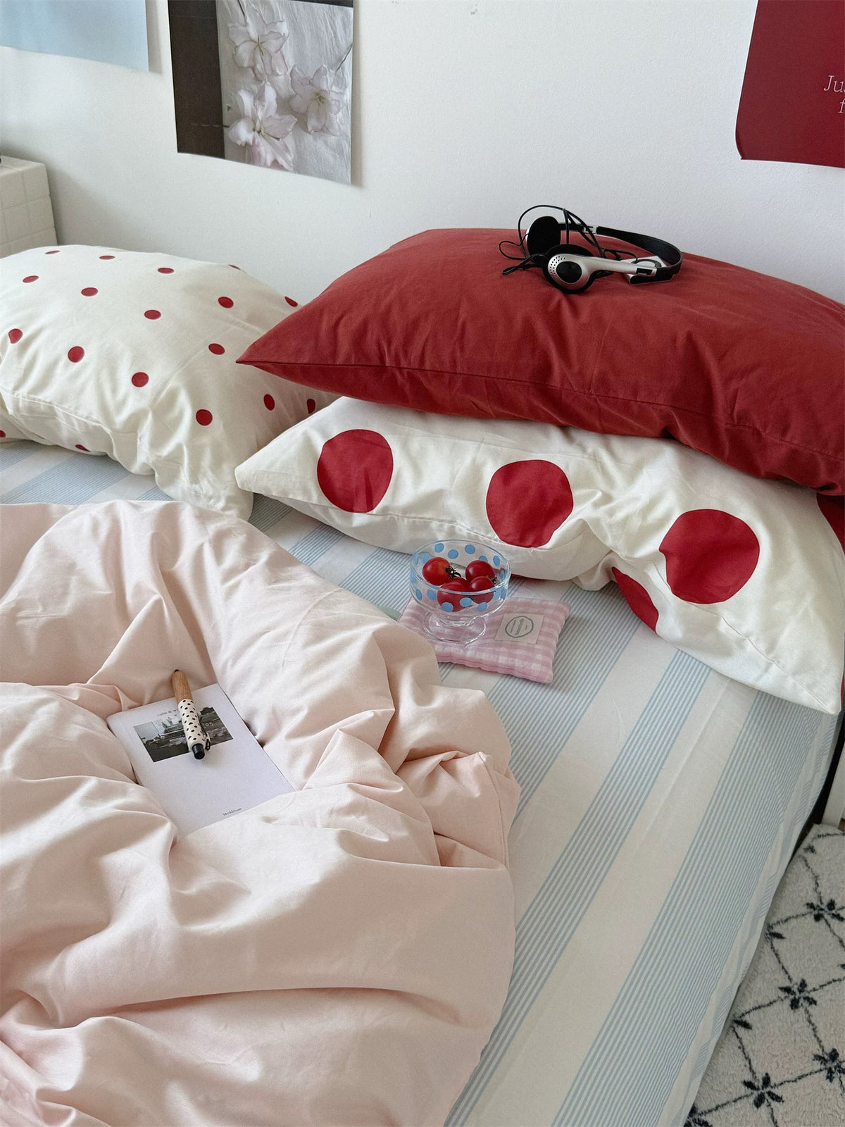 A red pillow and large red dot pillowcase sit above pink preppy bedding beside a white shelf.